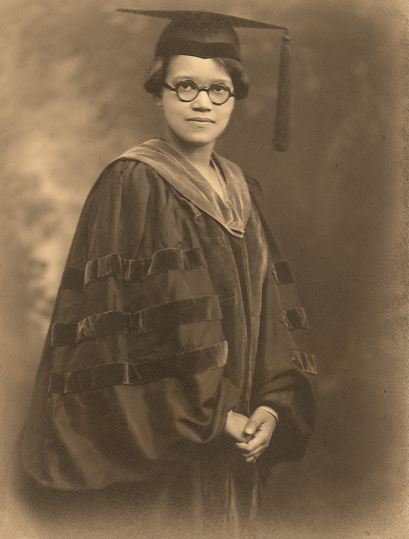 Historic sepia-toned portrait of Dr. Sadie Tanner Mossell Alexander wearing academic regalia and a graduation cap. She stands confidently, hands clasped, symbolizing her pioneering achievements as the first African American woman to earn a Ph.D. in Economics and a law degree from the University of Pennsylvania.